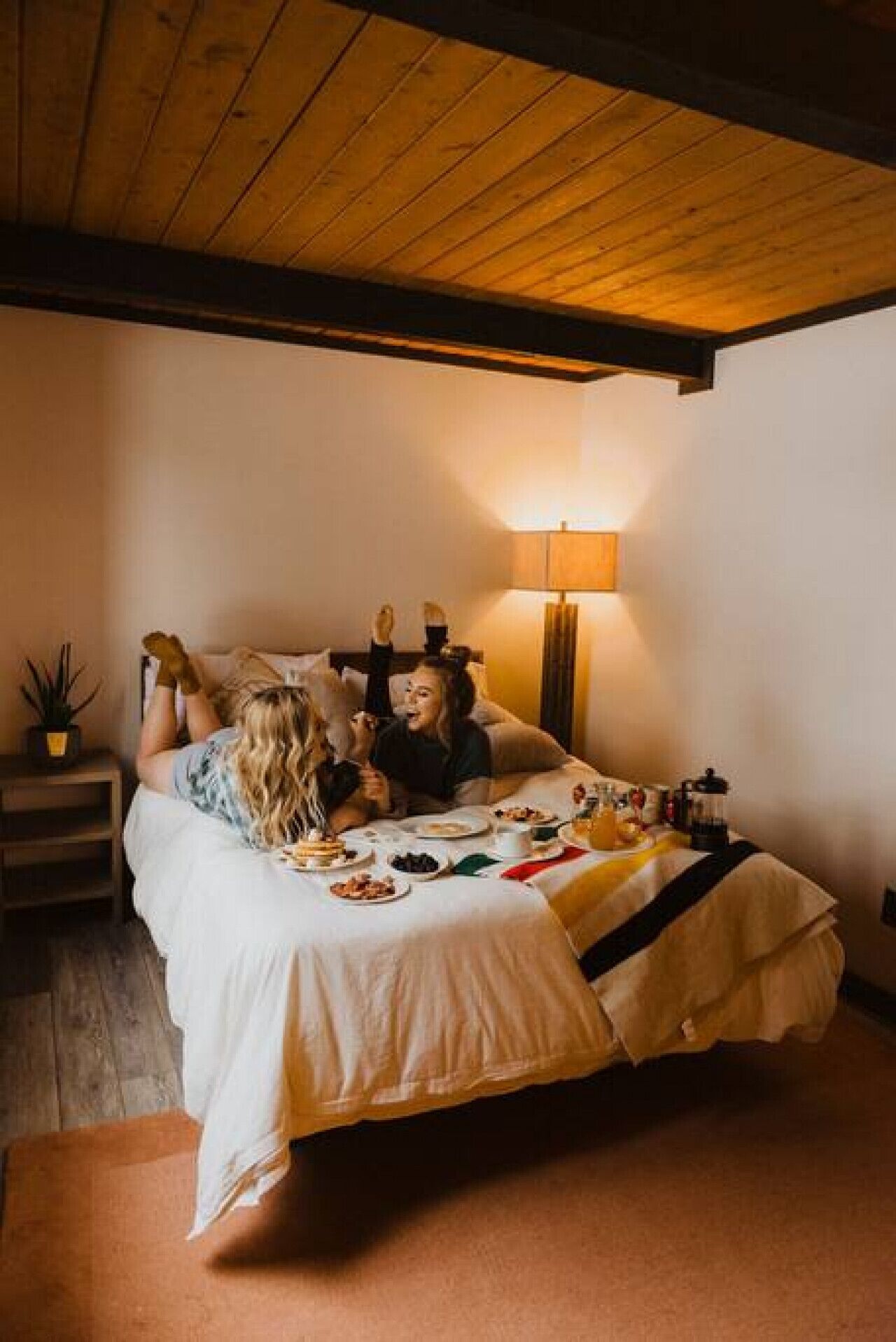 Een kamer met een bed, een nachtkastje, een lamp en een kleine plant in een pot.