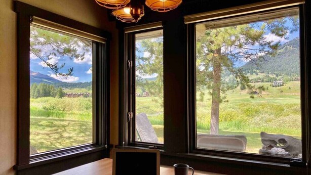 A room with a laptop on a table, large windows with a view of a green landscape and mountains. - Big Sky Bungalow - Center of Big Sky (Big Sky)