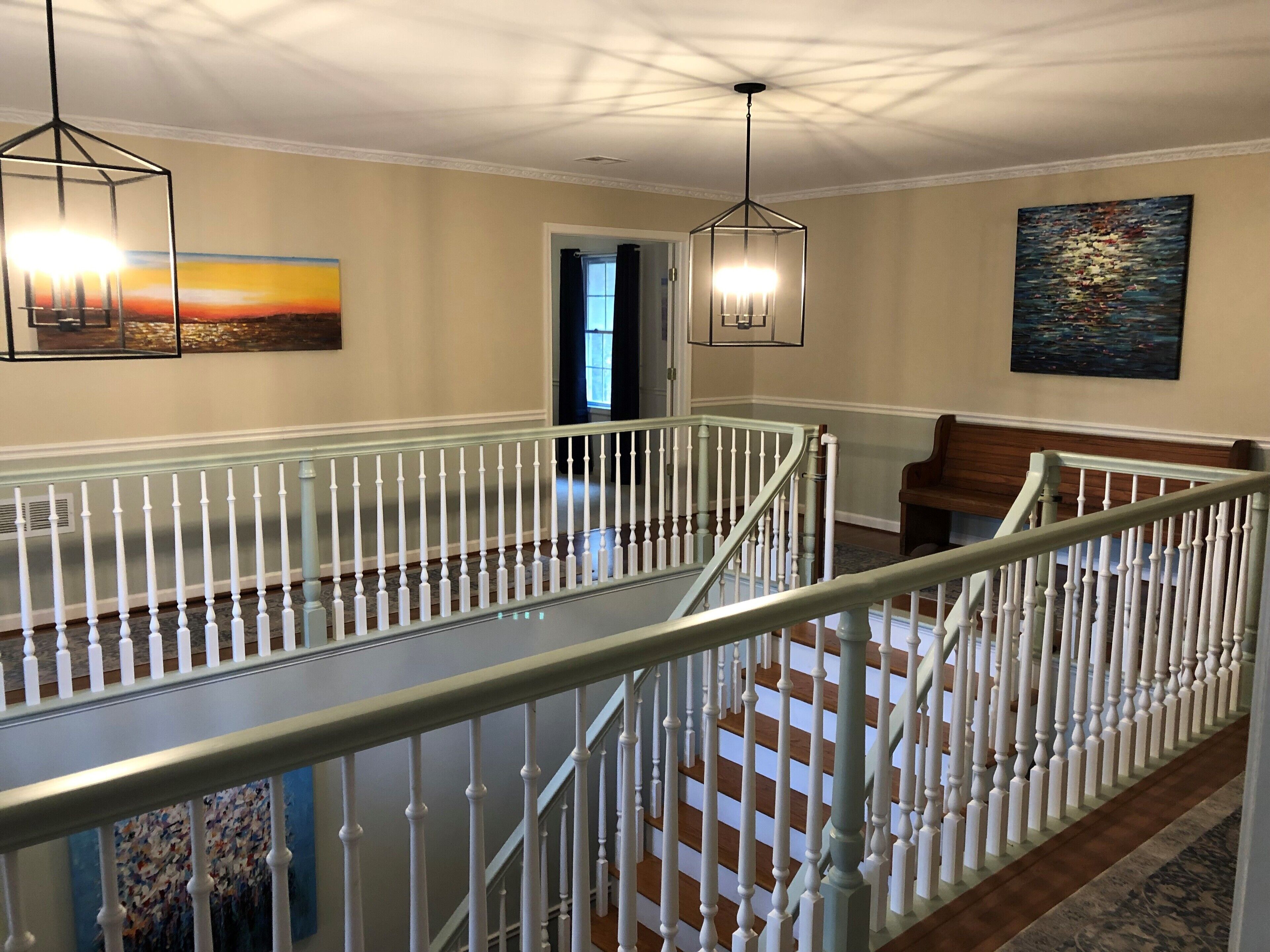 A spacious interior with a high ceiling, a staircase with white balusters, and a view of a sunset through a window.
