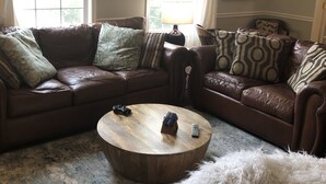 Een woonkamer met een bruine leren bank, een ronde houten salontafel en een zacht, wit tapijt.