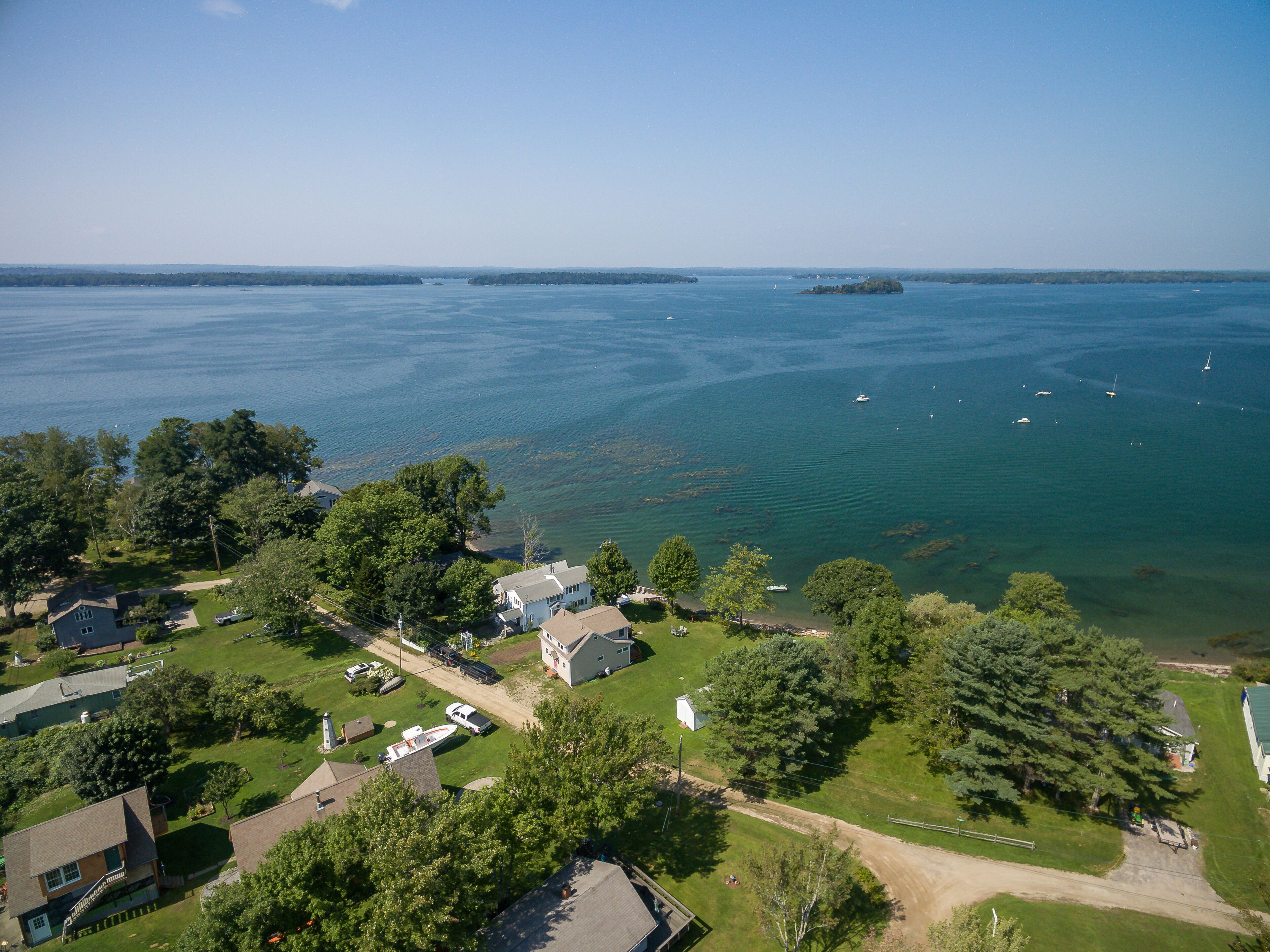 An aerial view of a coastal residential area with houses, a clear sky, and a calm sea with boats.