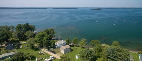 An aerial view of a coastal residential area with houses, a clear sky, and a calm sea with boats.