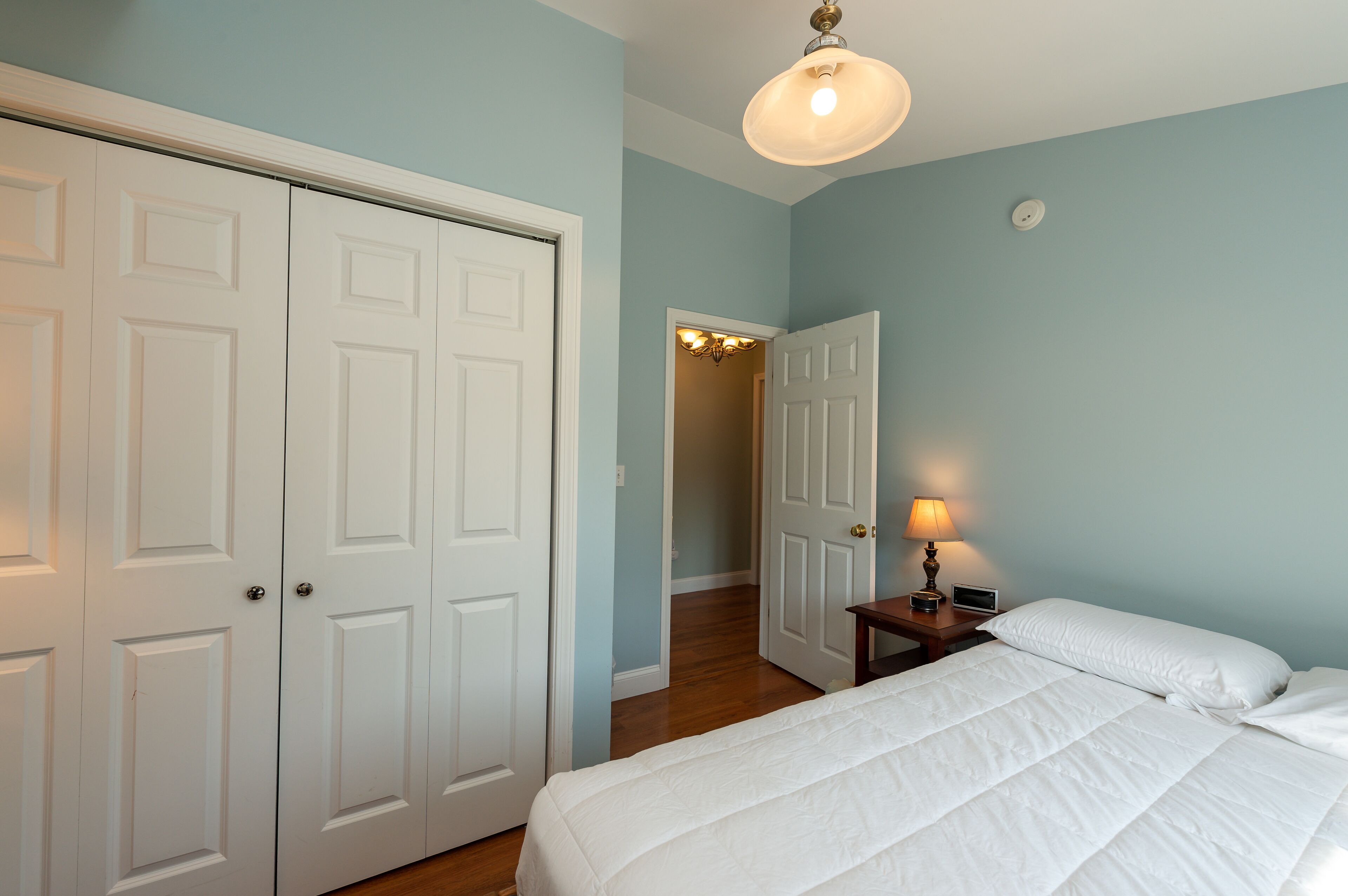 Une chambre à coucher comprenant un lit, une table de chevet, une lampe et une armoire à deux portes.