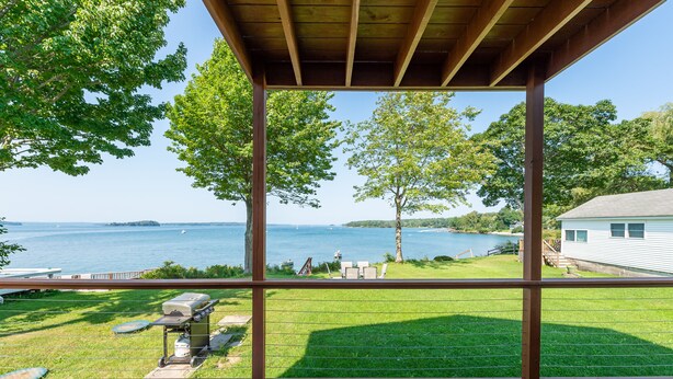 Une terrasse couverte avec vue sur un lac, une pelouse et une maison en arrière-plan.