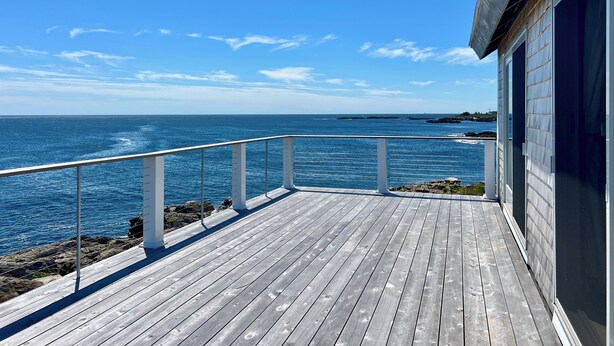 Une terrasse en bois avec une balustrade donnant sur l’océan, un bâtiment à l’extérieur sombre et une côte rocheuse.