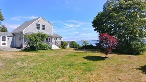 Une maison à deux étages avec un porche à l’avant, une petite terrasse et une vue sur une étendue d’eau.