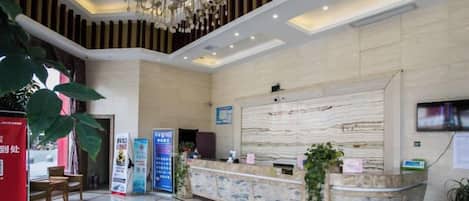 A hotel reception area with a marble reception desk, a chandelier, and a large plant.