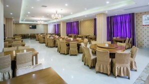 A spacious banquet hall with round tables and chairs, a chandelier, and purple curtains.