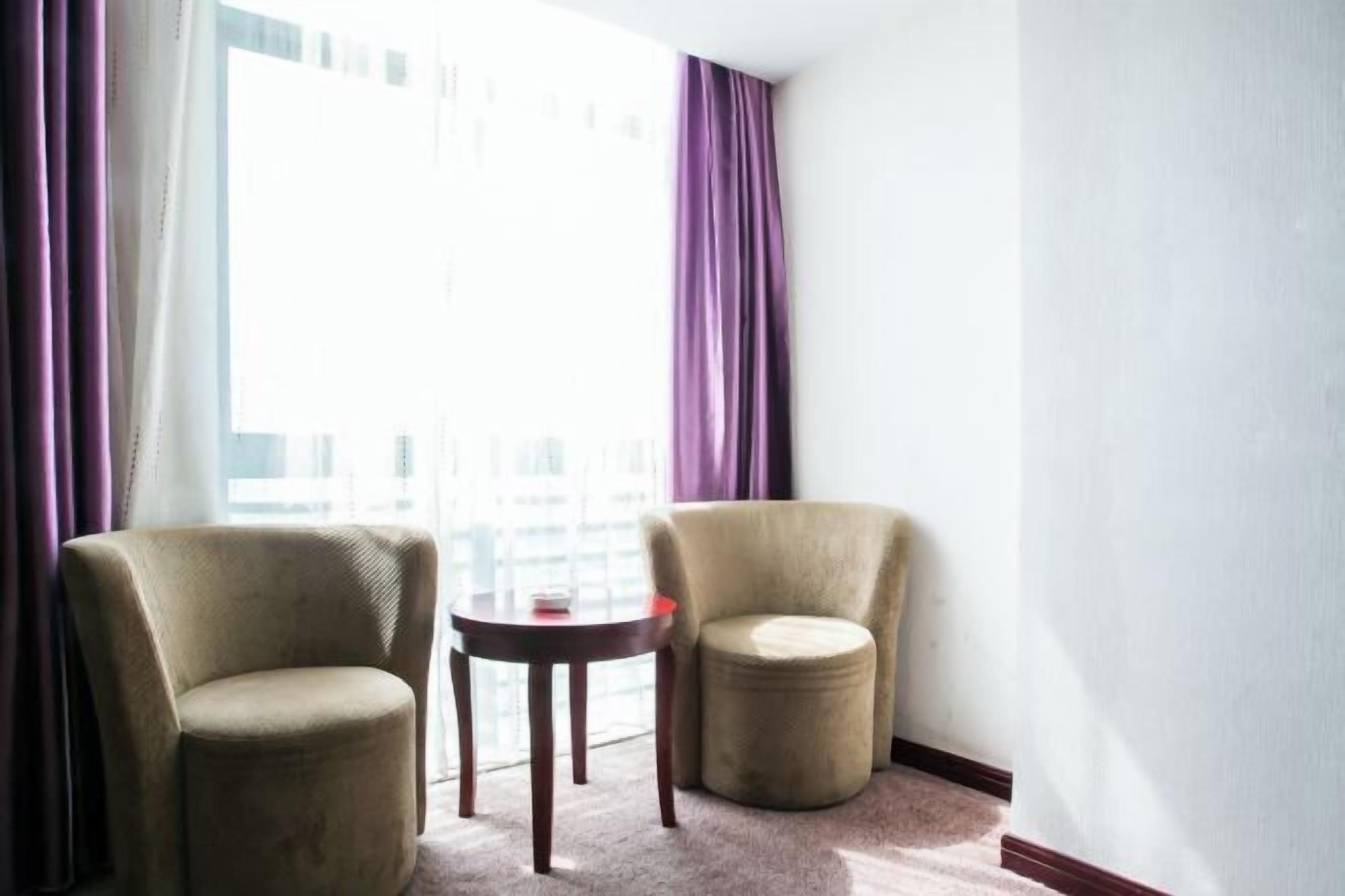 A hotel room with two armchairs, a small round table, and a large window with curtains.