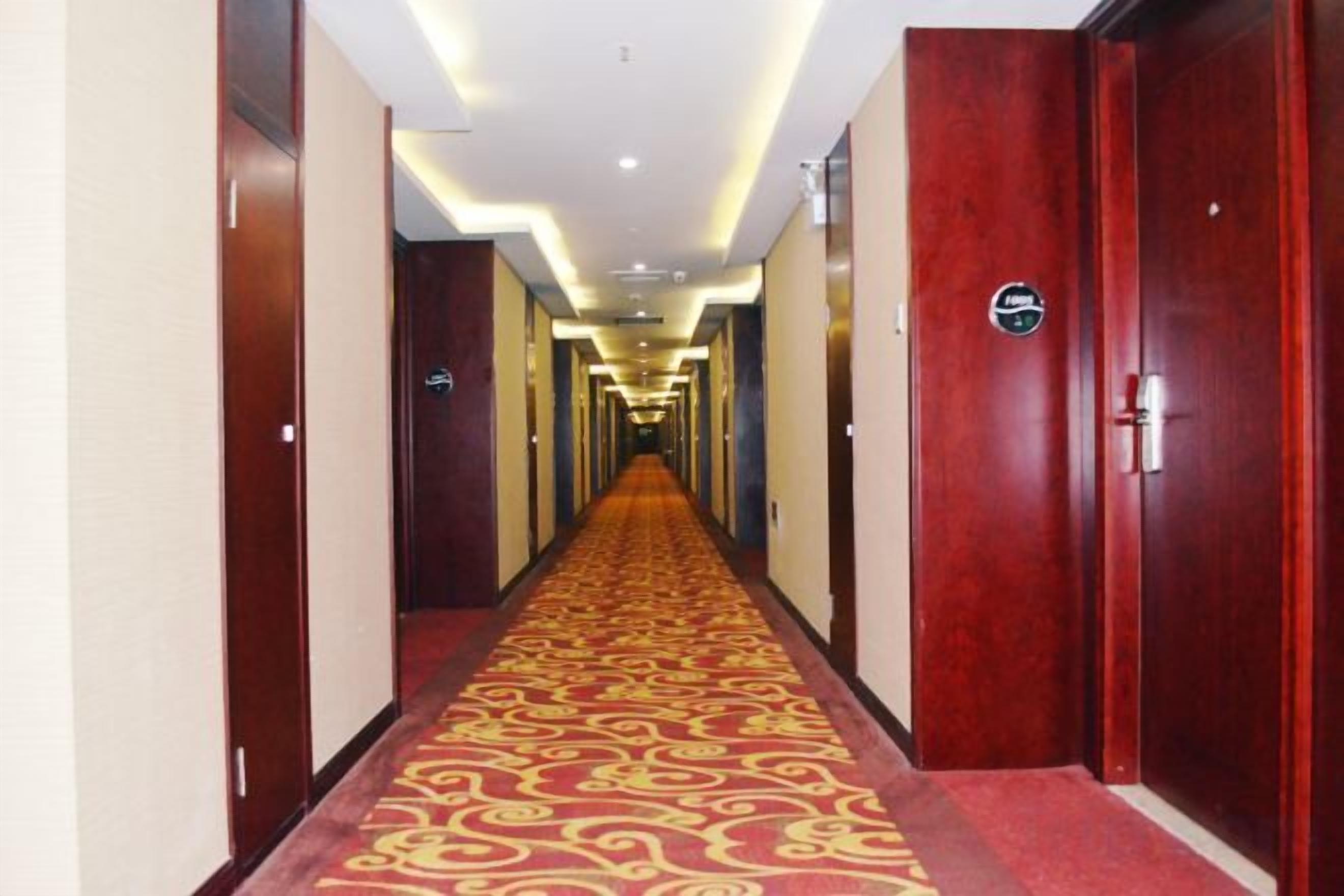 A hotel hallway with a carpeted floor, wooden doors, and a sign indicating the direction to the elevator.