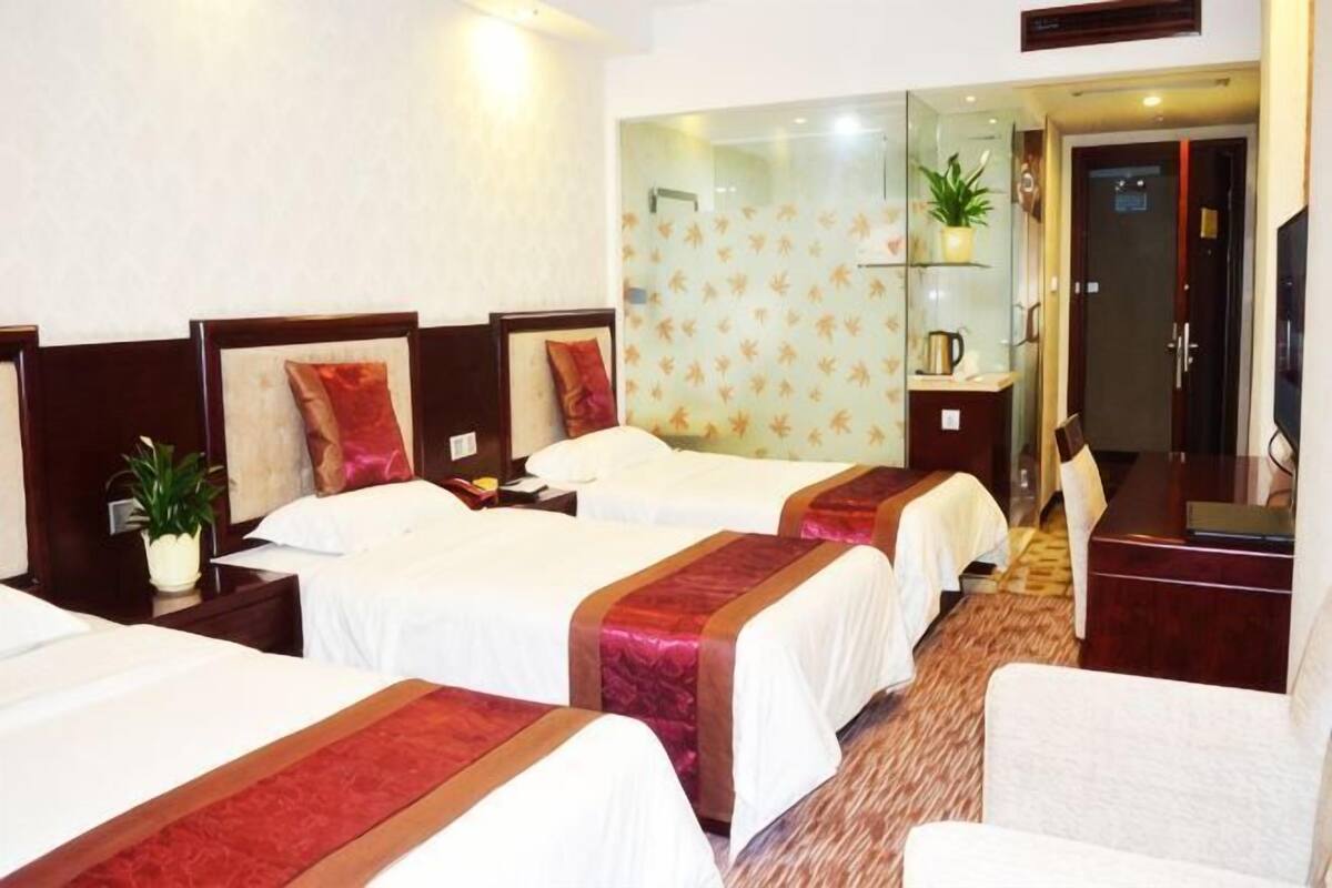 Une chambre d’hôtel avec trois lits, un canapé, une télévision et une petite plante.