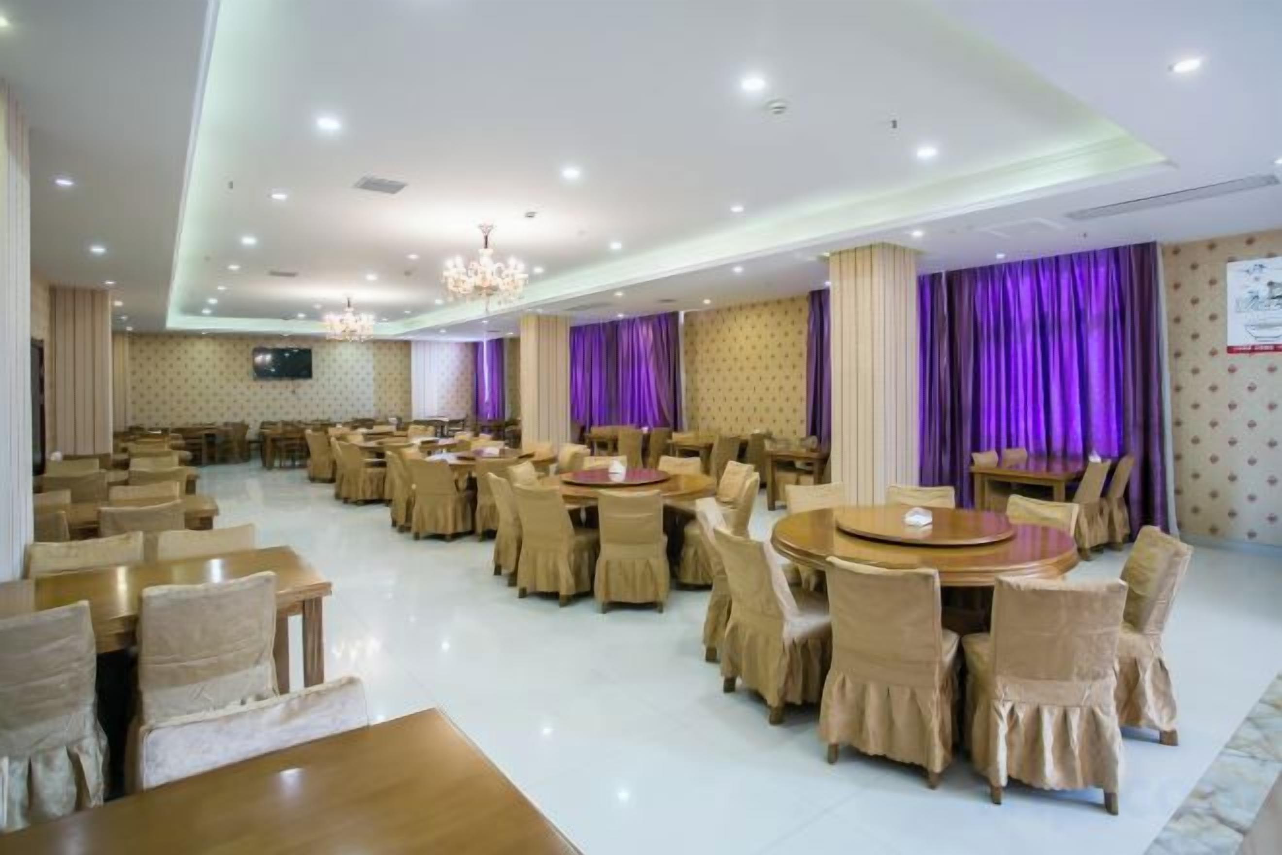 Un amplio comedor con varias mesas redondas y sillas, un candelabro y cortinas moradas.