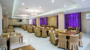 Un amplio comedor con varias mesas redondas y sillas, un candelabro y cortinas moradas.