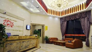 A hotel lobby with a reception desk, seating area, and a large chandelier.