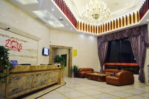 A hotel lobby with a reception desk, seating area, and a large chandelier.