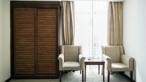 A hotel room with a sliding door, two armchairs, a small table, and a view through a window with curtains.