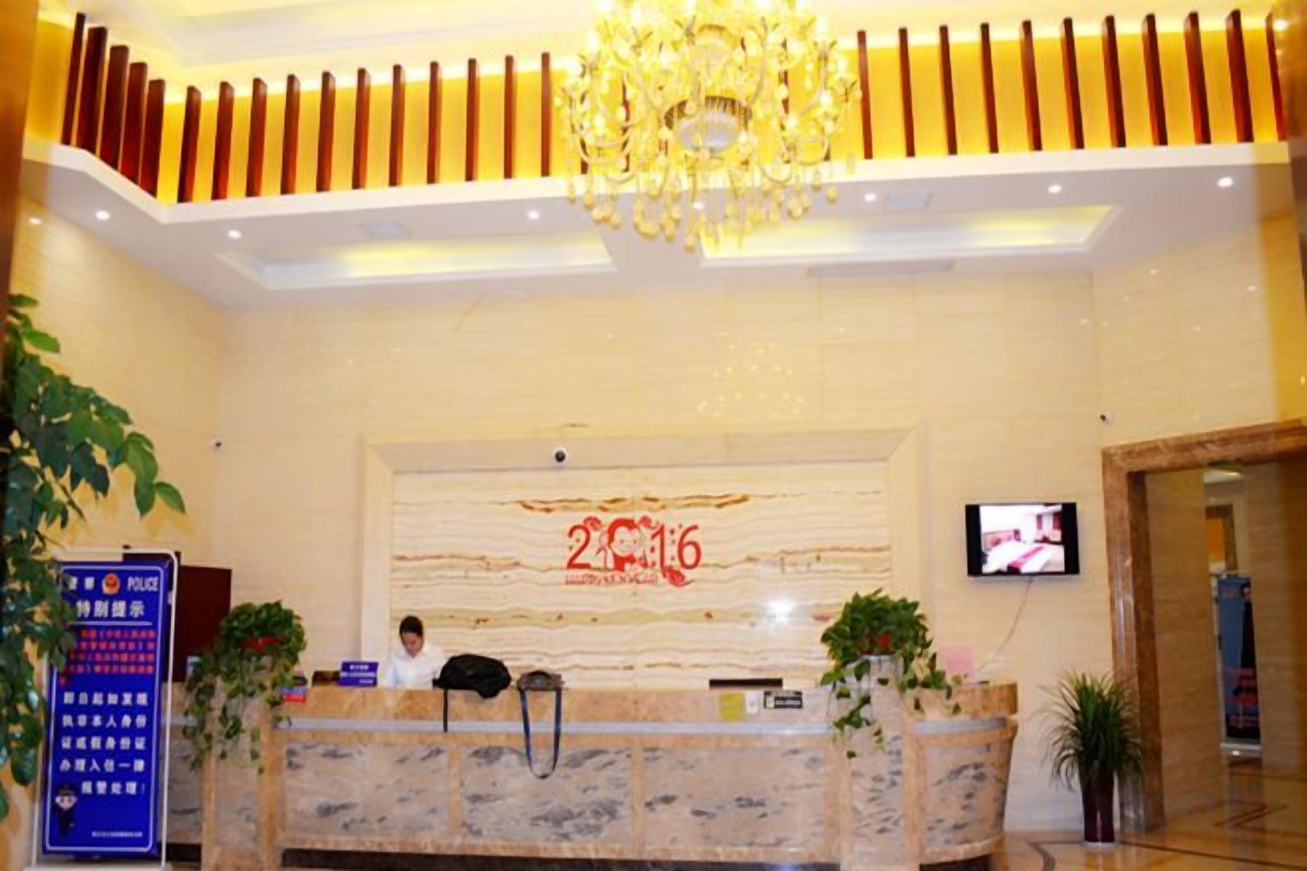 A hotel reception area with a marble counter, a television screen, and a chandelier.