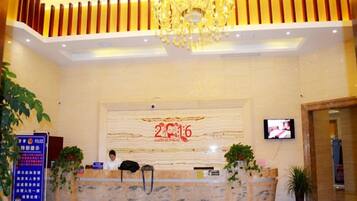 A hotel reception area with a marble counter, a television screen, and a chandelier.