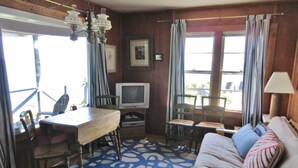 Een gezellige kamer met een houten vloer, een bank, een televisie en een eettafel met stoelen.