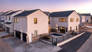 A modern residential area with houses featuring sloped roofs, white exteriors, and a swimming pool.
