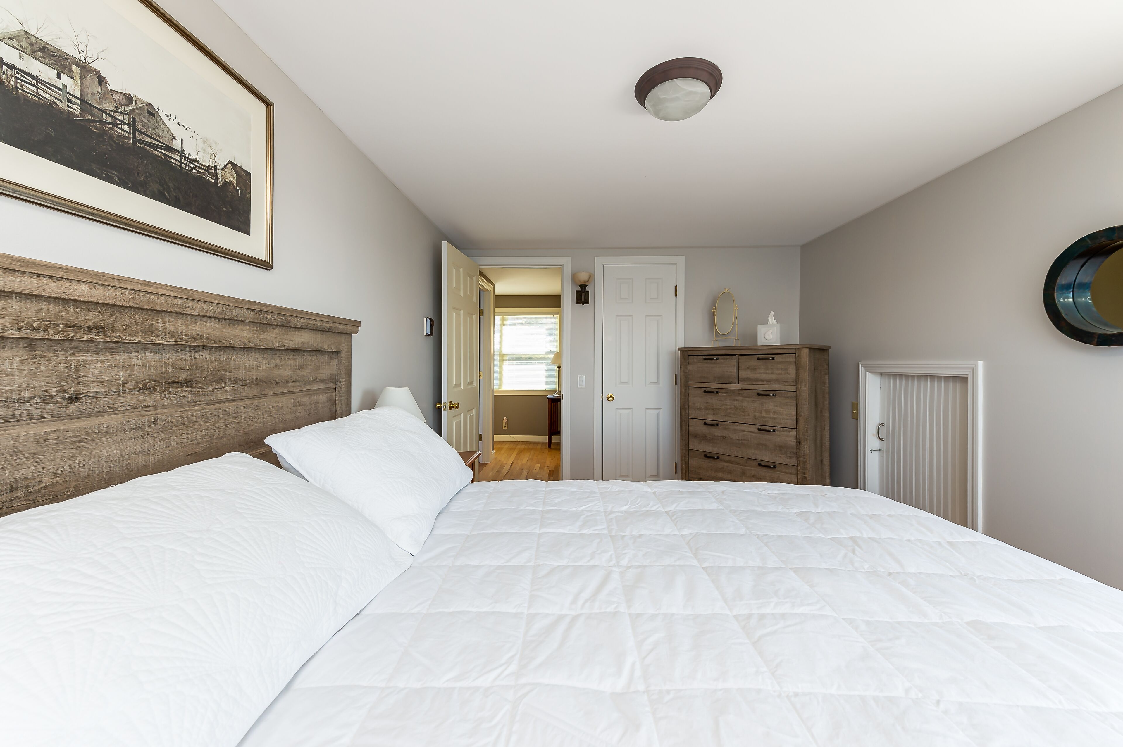 A bedroom with a large bed, wooden headboard, a dresser, and a framed picture on the wall.