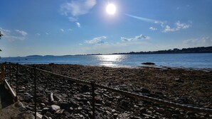 Une plage rocheuse, délimitée par une barrière faite de cordes, avec une eau calme et un ciel dégagé.