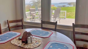 A dining area with a table set for four, a window with a view of outdoor furniture and a grassy area. - Thorburn - Experience a classic ME vacation at this beautiful summer cottage (Harpswell)