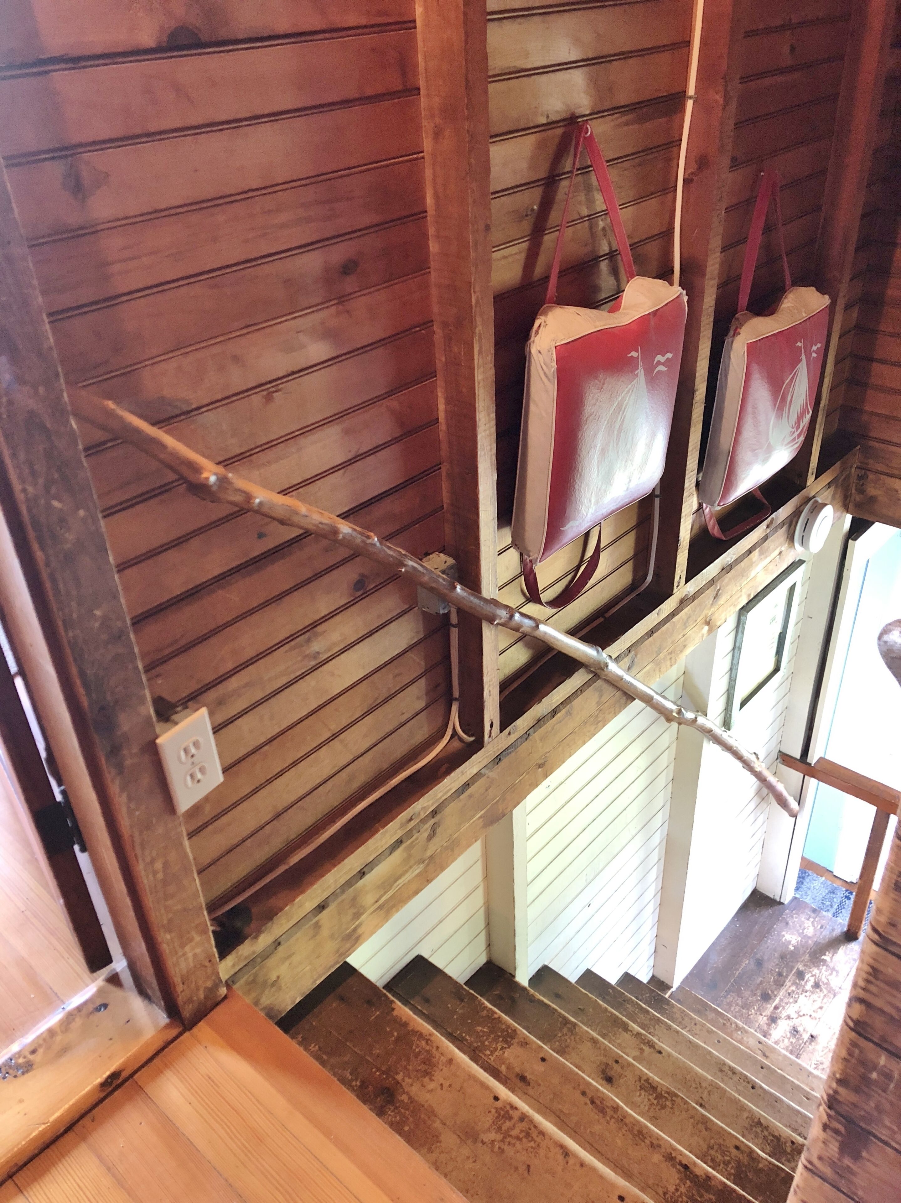 Eine Holzt Treppe mit Handlauf, eine Holzwand mit horizontalen Planken und eine weiße Tür am unteren Ende.