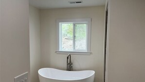 A bathroom with a freestanding bathtub, a window above the tub, and a light switch on the wall. - New Home on 5 acres, Clean, Quiet Comfortable with Private Dog Park (Columbus)