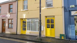 A row of buildings with distinct yellow and blue facades, including a shop with a visible sign. - Glebe House (Ballinrobe)