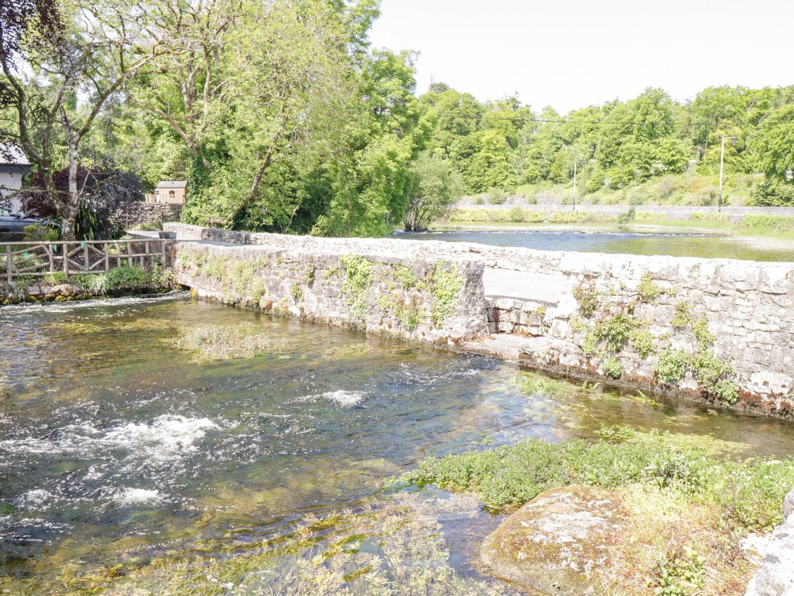 Un pont de pierre enjambe une rivière aux eaux claires, dont les rives sont bordées de verdure.