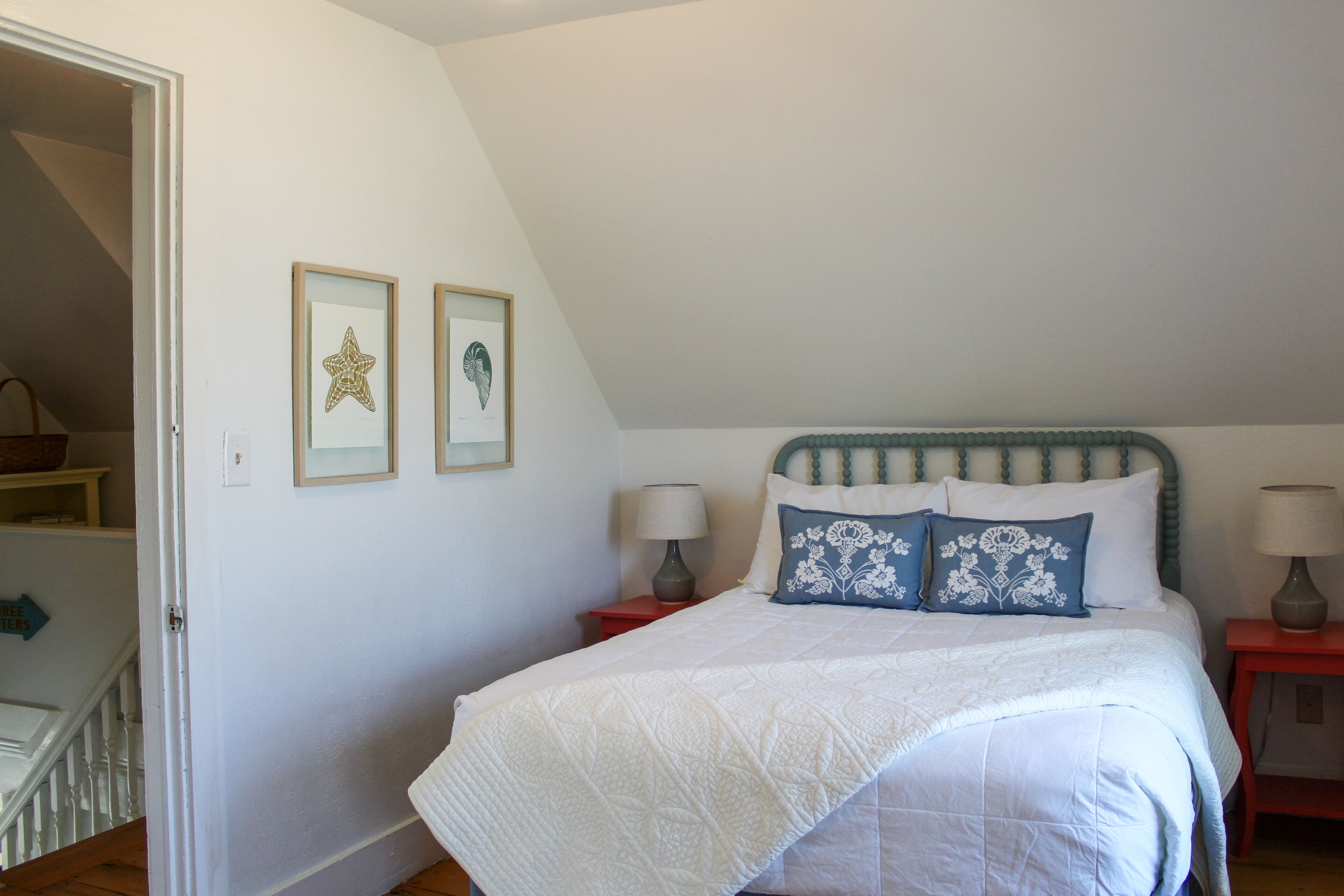 A bedroom with a bed, two bedside tables, and a door leading to a staircase.
