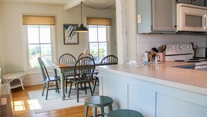 Une cuisine dotée d’un îlot central, de chaises en bois, d’une table à manger et offrant une vue dégagée grâce à de grandes fenêtres.