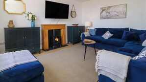 A living room with a fireplace, a blue sofa, a television, and a chandelier. - Ael Y Fron (Pwllheli)