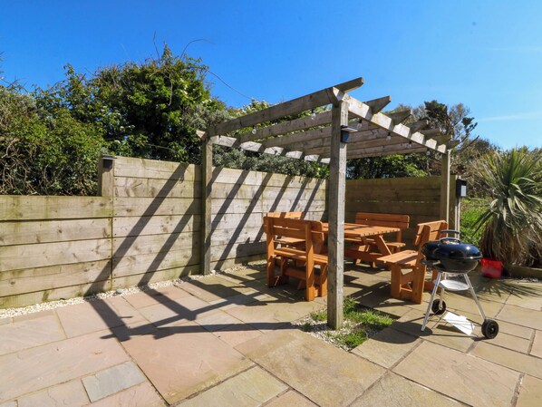 A wooden pergola with seating, a barbecue grill, and a potted plant.