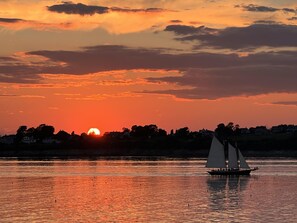 Un coucher de soleil sur une étendue d’eau, avec un voilier à l’horizon.