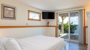 A bedroom with a bed, a television, a window, and a view of the outdoors. - Sunset Cottage - Capture Breathtaking Sunsets from this Beautiful Home (Bailey Island)