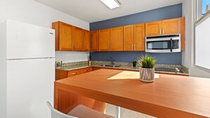 A modern kitchen with wooden cabinets, a granite countertop, a built-in microwave, and a potted plant. - Puerto Rico Ocean Park Beach Vacation Rental Otium Rentals (San Juan)