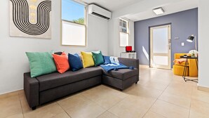 A modern living room with a grey sectional sofa, colorful cushions, and a large abstract painting. - Puerto Rico Ocean Park Beach Vacation Rental Otium Rentals (San Juan)