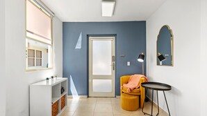 A hallway with a white console table, a yellow chair, a small round table, a door, and a mirror on the wall. - Puerto Rico Ocean Park Beach Vacation Rental Otium Rentals (San Juan)