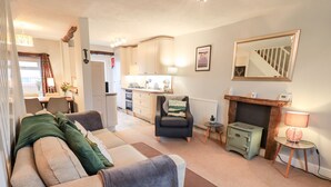A cozy living room with a sofa, a chair, a fireplace, and a kitchen in the background. - The Old Betting Shop (Keswick)