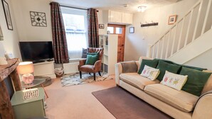 A living room with a sofa, armchair, TV, and a staircase. - The Old Betting Shop (Keswick)