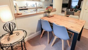 A modern kitchen with a wooden island, two blue chairs, a dining table, and a black chair with a woven seat. - The Old Betting Shop (Keswick)