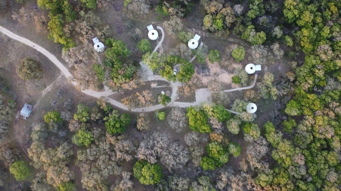 An aerial view of a forested area with four circular structures, possibly cabins or huts, connected by winding paths.