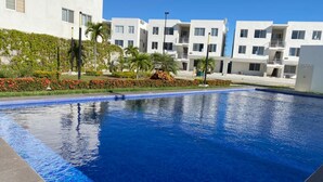 Una piscina circondata da edifici moderni con balconi, cielo sereno e verde curato.