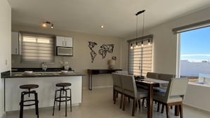 Una cucina moderna con zona pranzo, caratterizzata da una grande isola con sgabelli, un tavolo da pranzo con sedie e vista sull'esterno tramite ampie finestre.