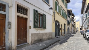 A narrow cobblestone street lined with historic buildings, featuring wooden doors and green shutters.