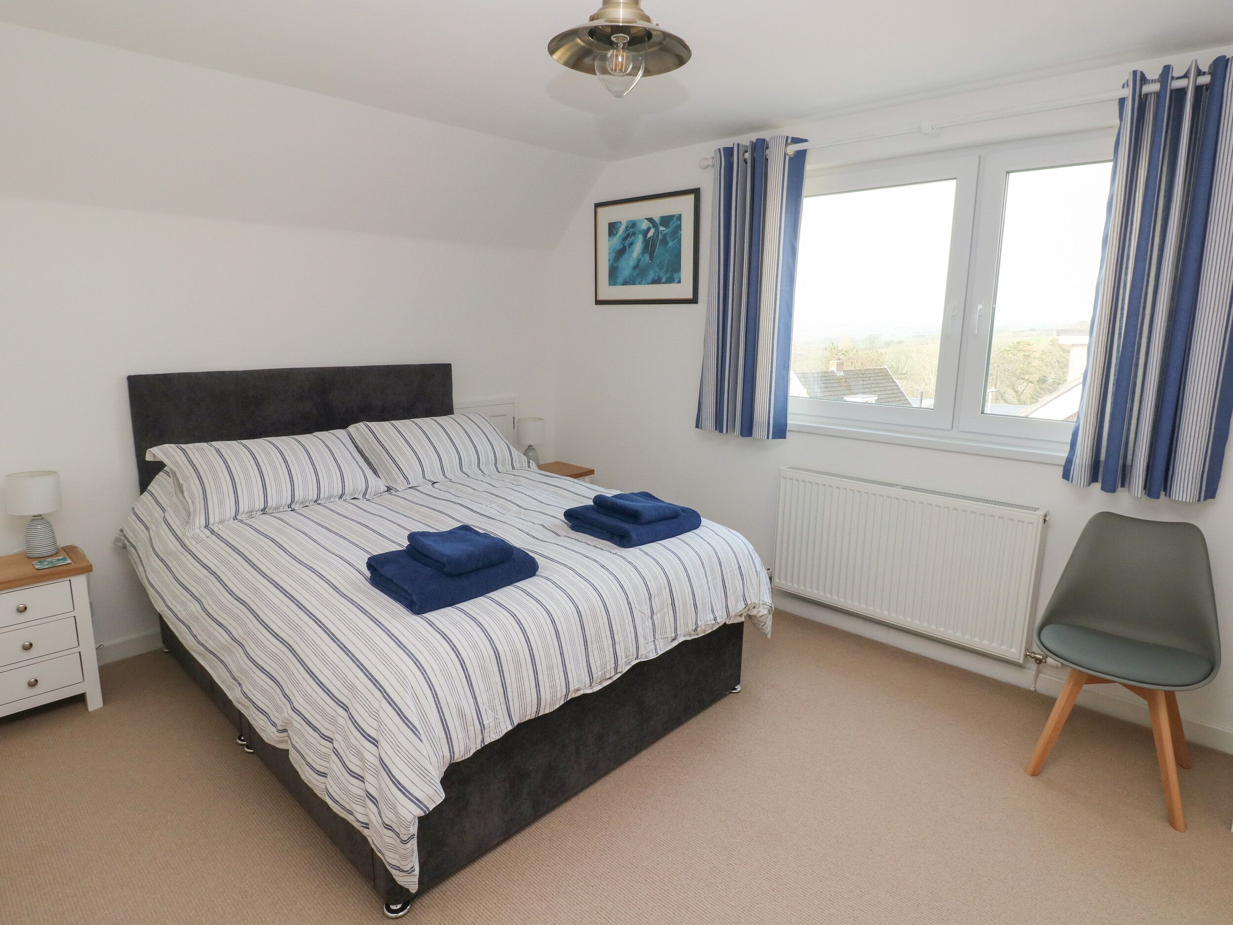 A bedroom with a bed, a nightstand, a chair, a window with curtains, and a radiator.