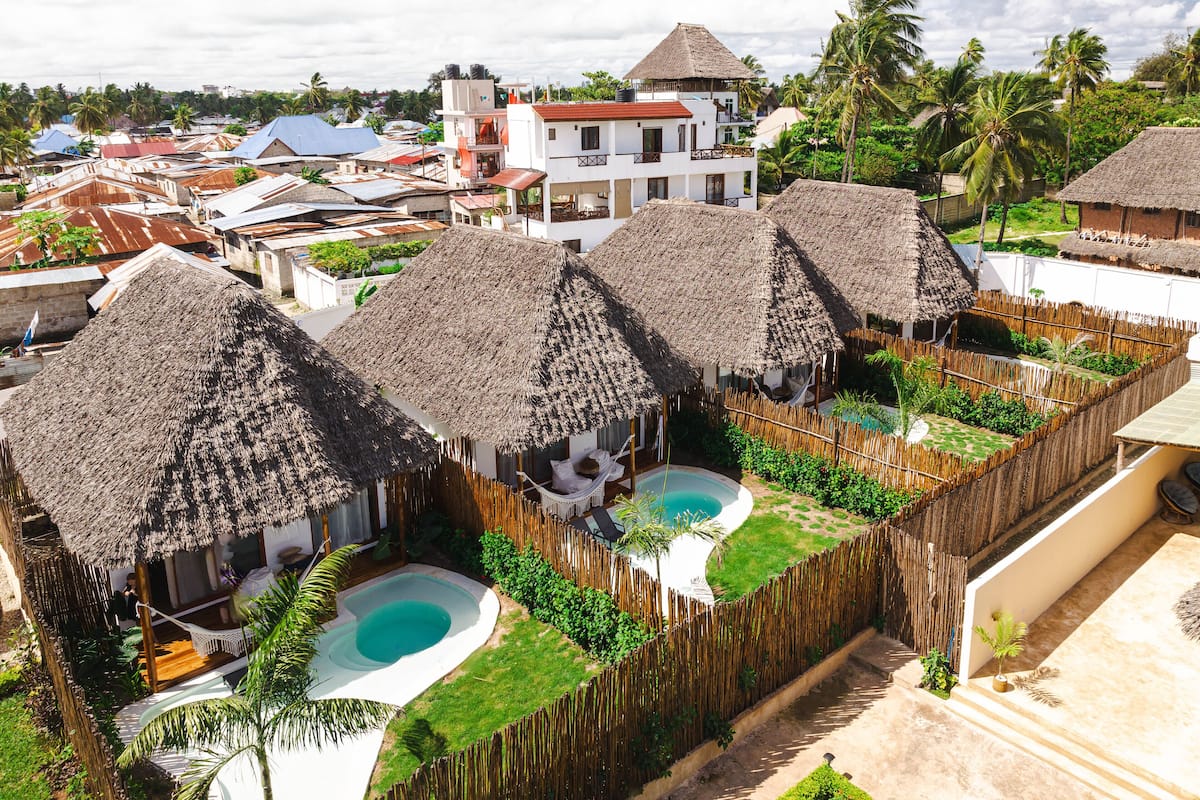 A resort with thatched-roof huts, a swimming pool, and lush greenery.