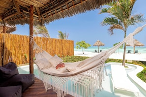 Een hangmat met macramé franje, een houten terras, een zwembad en uitzicht op het strand.